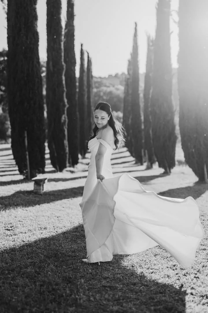 Sposa che fa volteggiare l'abito in un viale di cipressi, fotografia di matrimonio in bianco e nero in Toscana